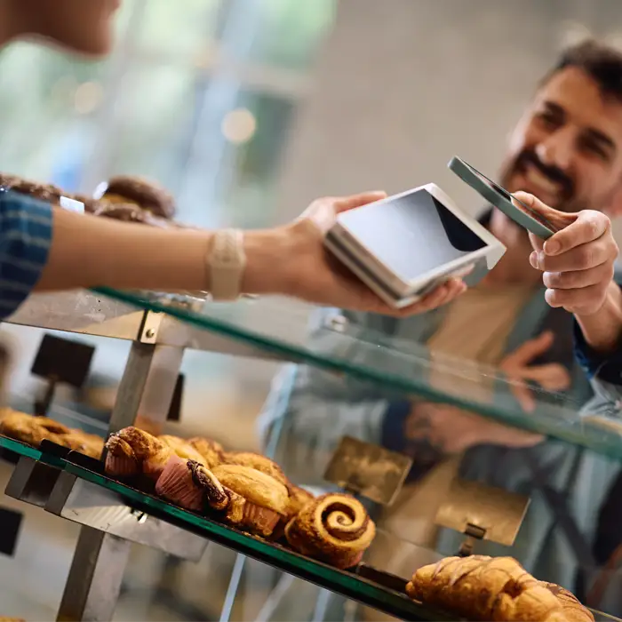 Customer using tap pay on a mobile reader at a bakery Customer using tap pay on a mobile reader at a bakery